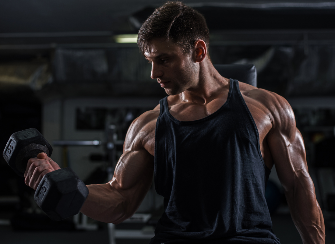 Muscular man doing bicep curls with a serious expression in the gym